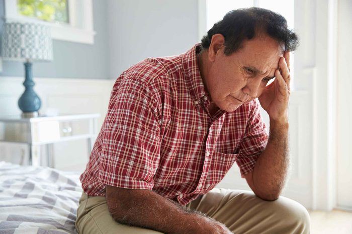 Man sitting on bed with hand on his head