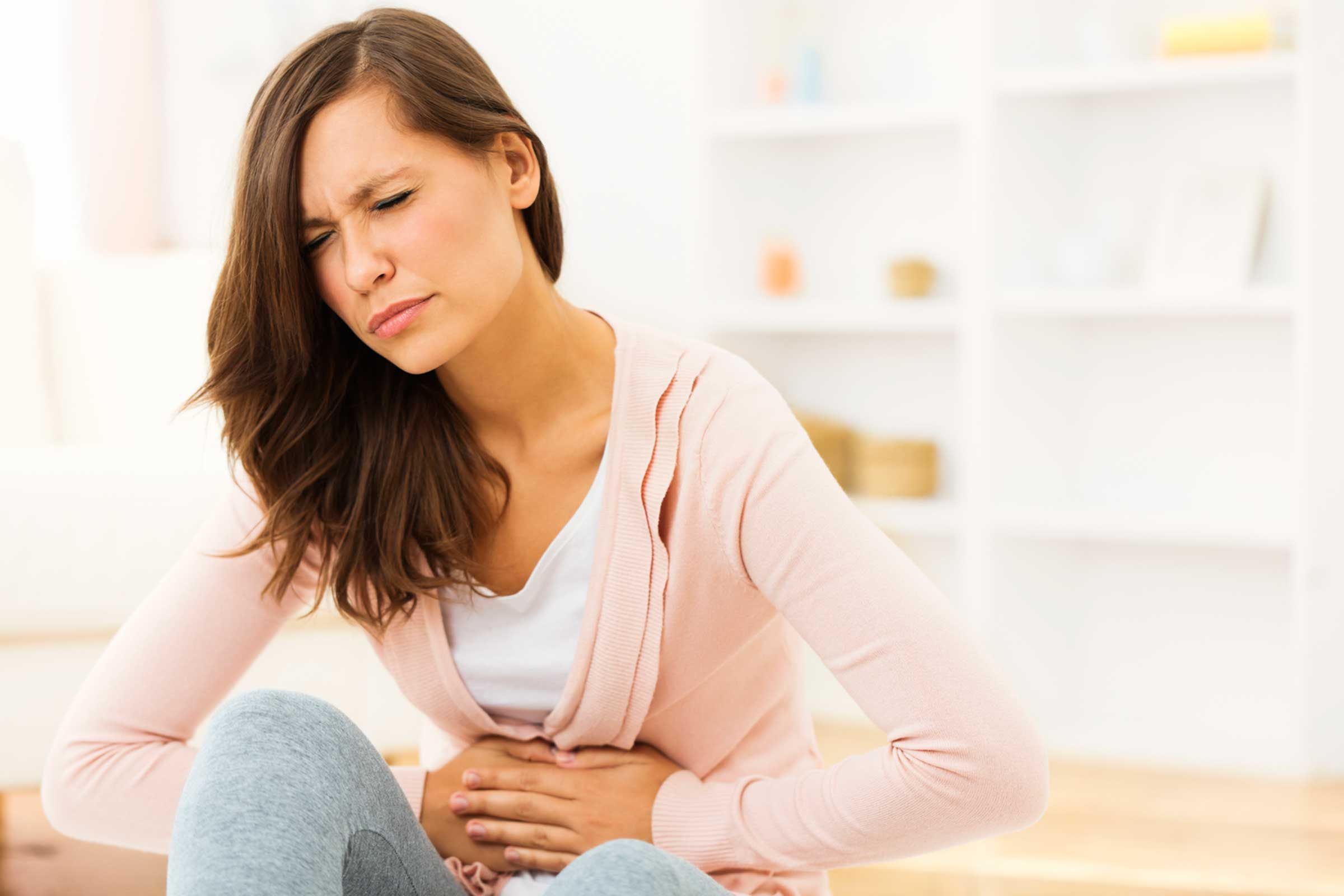 woman wincing in pain with her hands crossed on her stomach