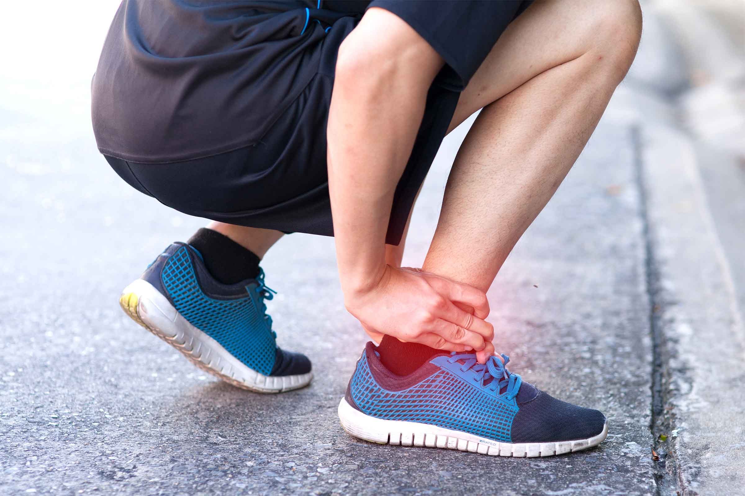 person bending down and clutching their ankle