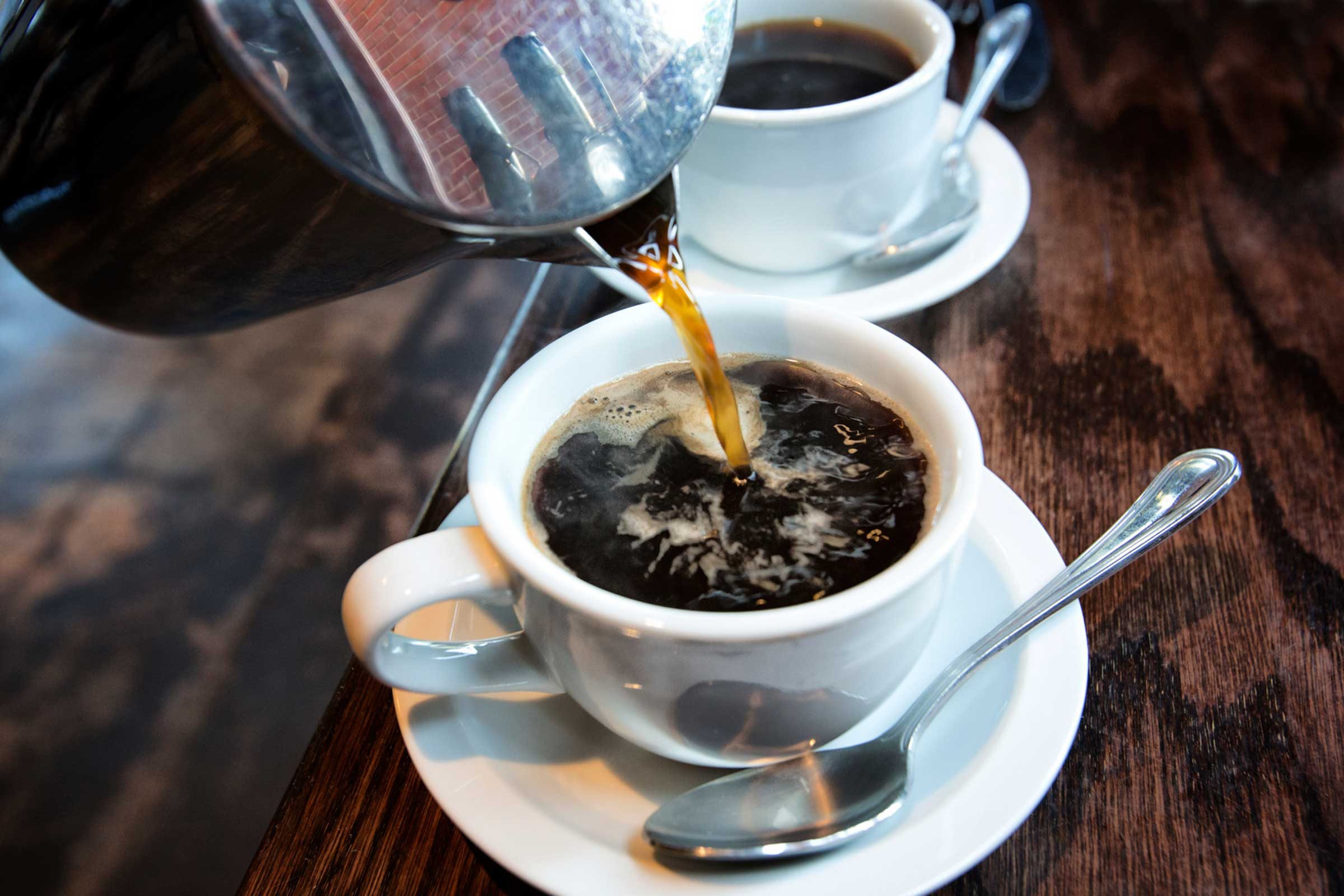 coffee pot pouring into a white cup and saucer