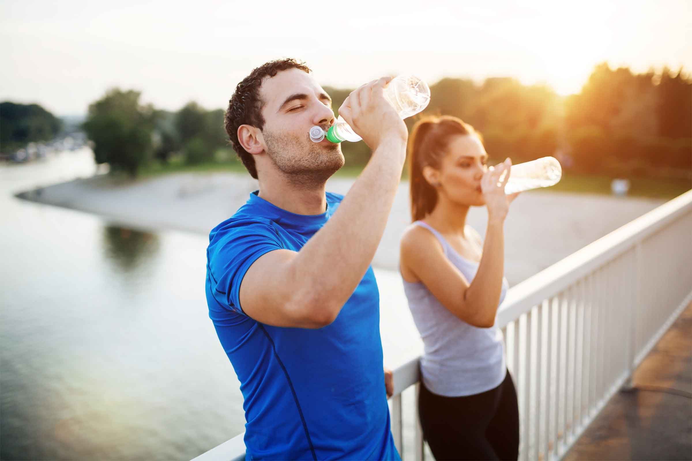 Exercising man and woman stop on a footbridge over a body of water to drink from their water bottles.
