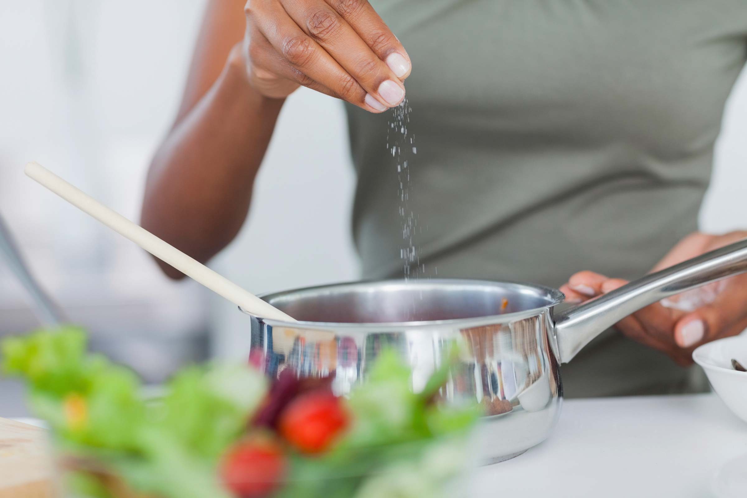 Woman sprinkling salt into a pot.