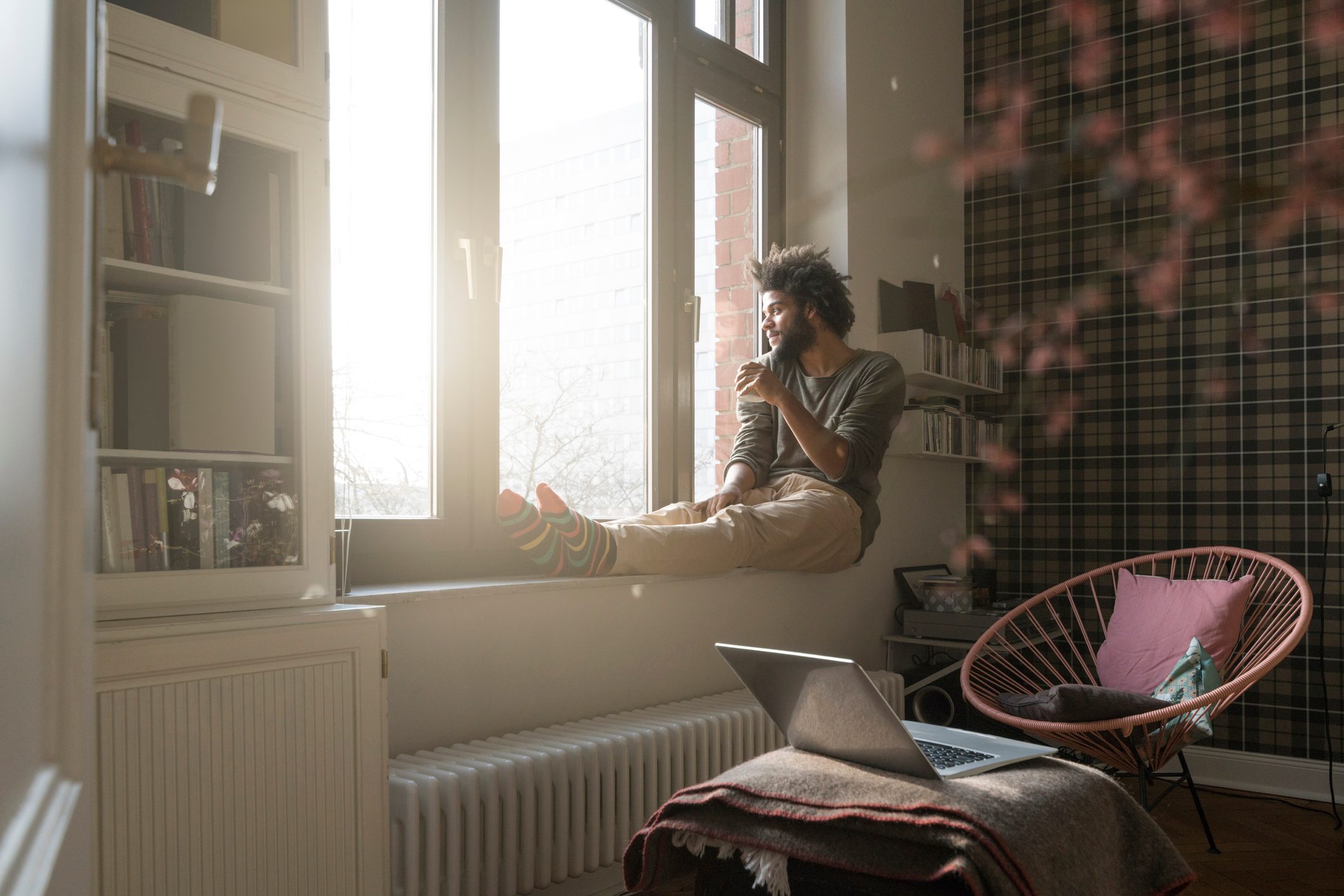 man sitting on window sill in living room looking outside