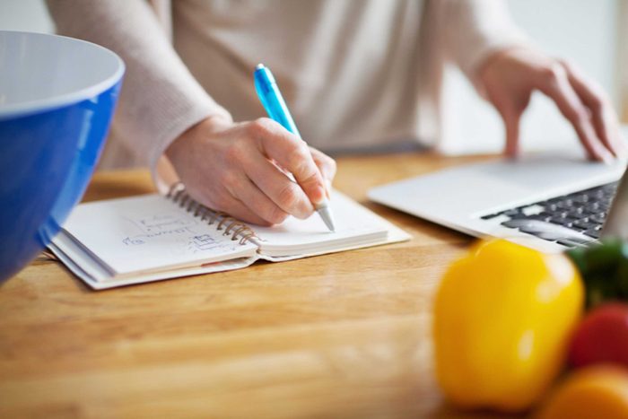 Woman writing in journal and using laptop