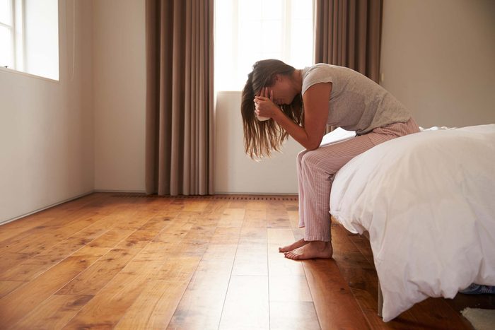 distraught woman holding her head in her hands and sitting on a bed