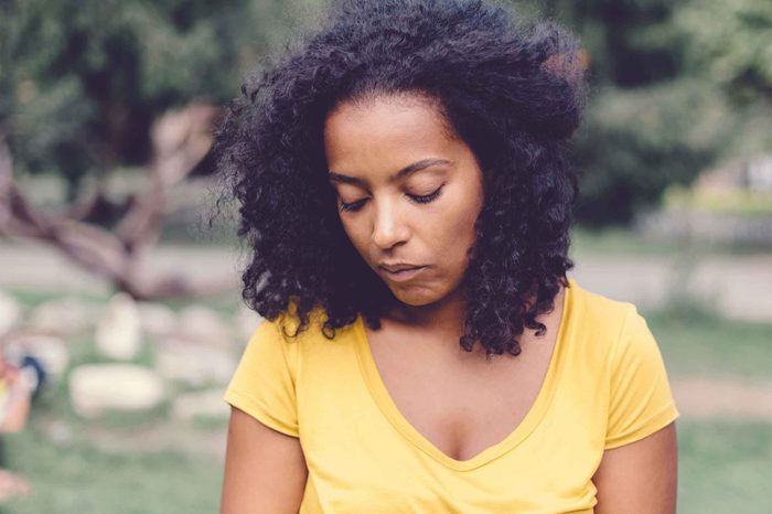 Woman in a yellow shirt standing in a park and looking depressed.