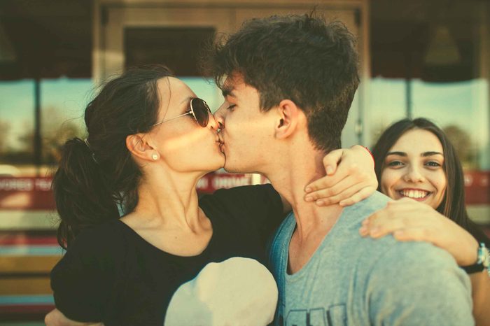 Man and woman kissing while another woman stands in the background.