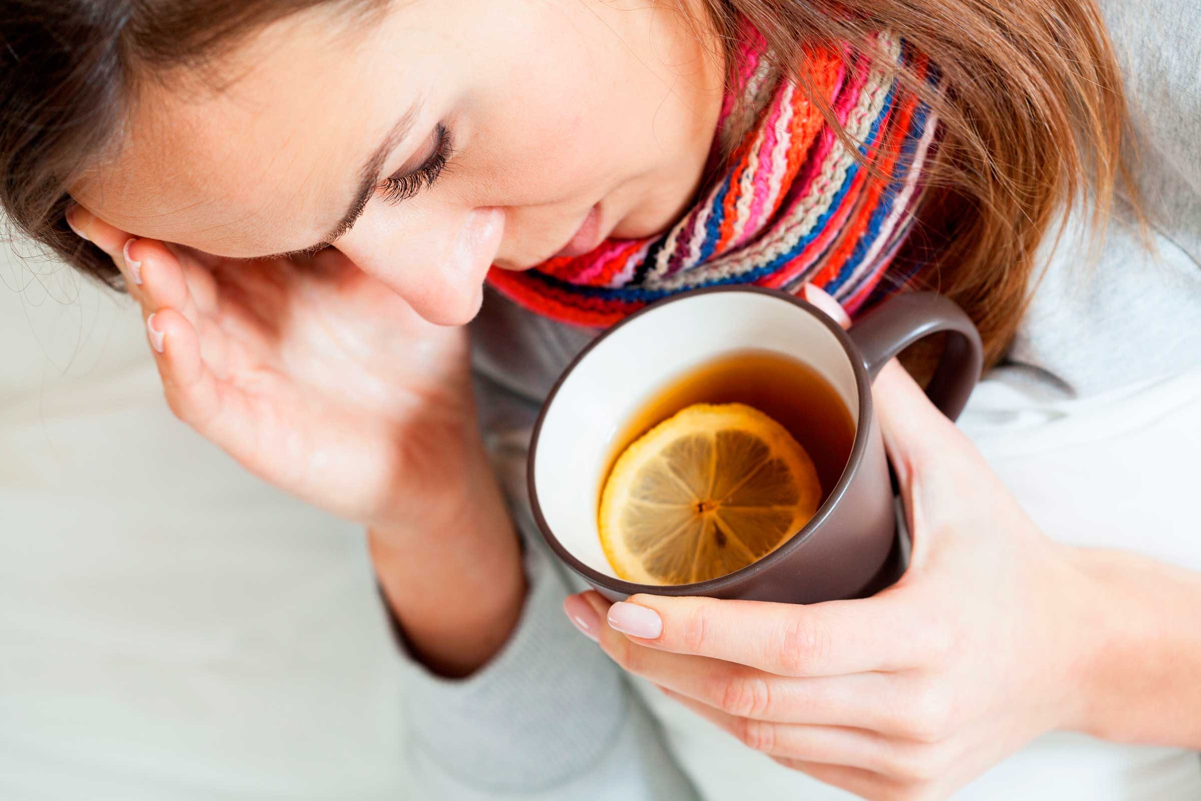 woman holding mug of tea with lemon with one hand and forehead with the other