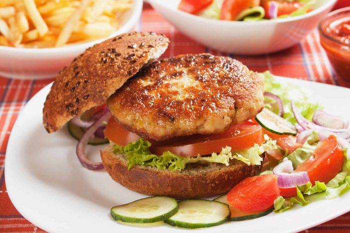 Veggie burger and hamburger bun on a picnic table and plate full of cucumbers, tomatoes, and onions.