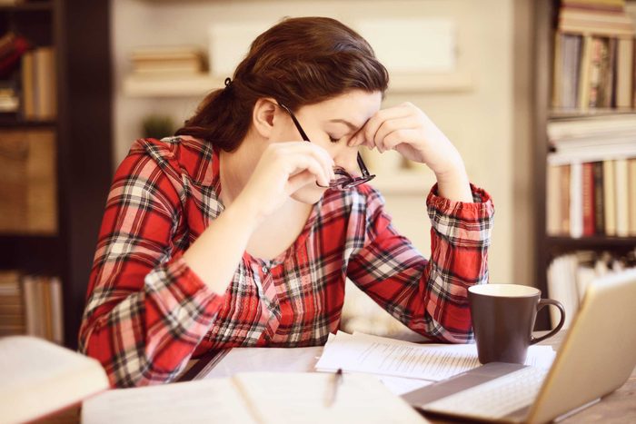 tired woman holding the bridge of her nose in front of a laptop