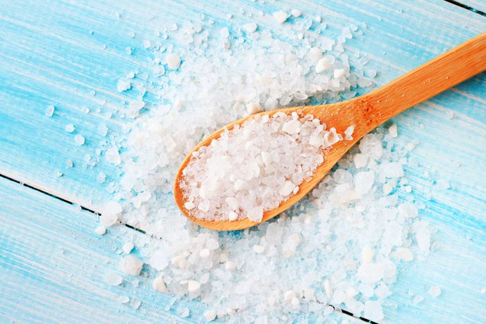 Wooden spoon spilling over with sea salt.