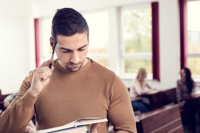 man looking at a book holding a pen to his temple
