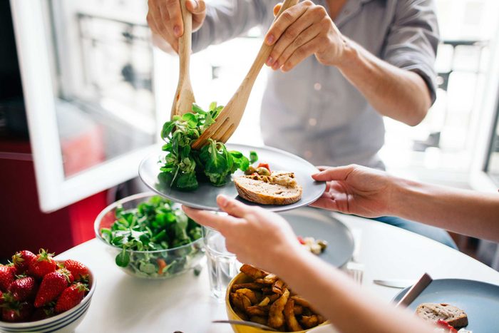 person serving salad onto another person's plate