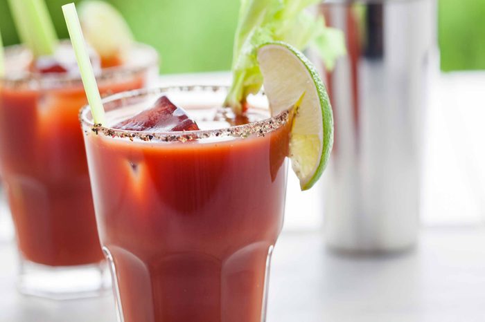 Two Bloody Mary alcoholic drinks on a table near a shaker cup.