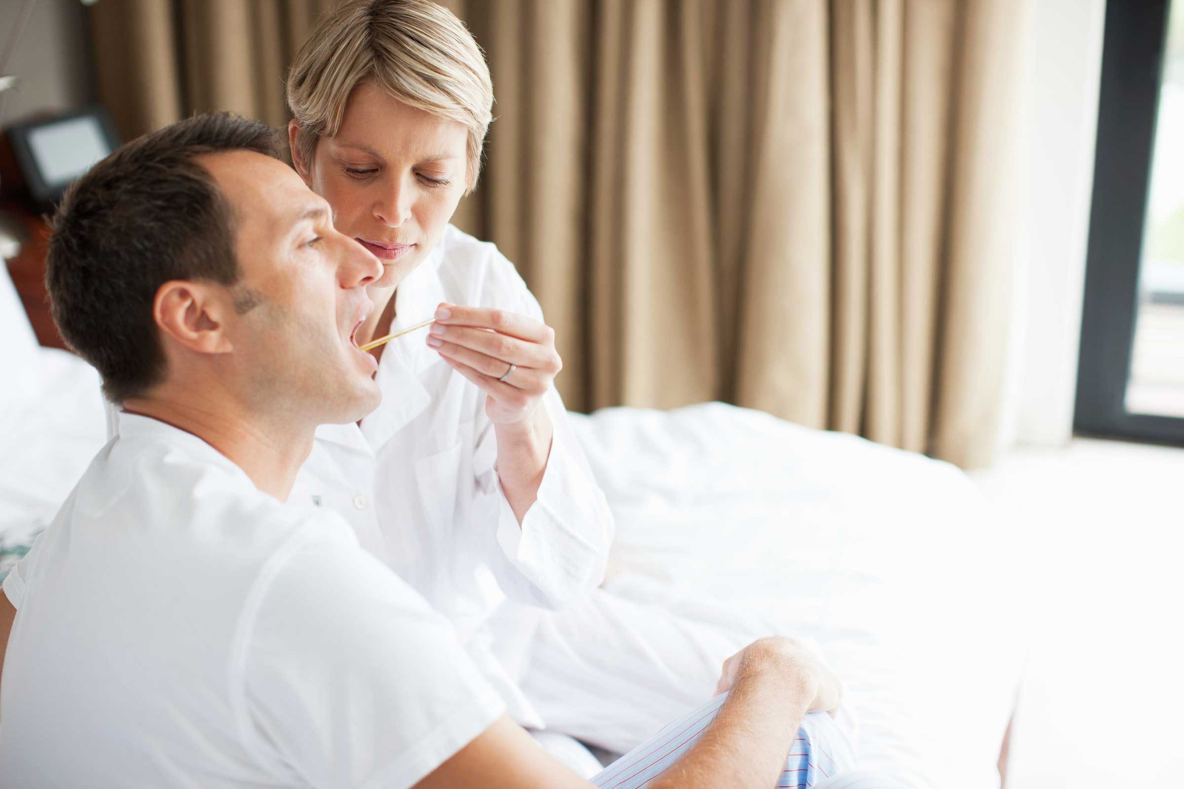 woman checking a man's temperature with a thermometer