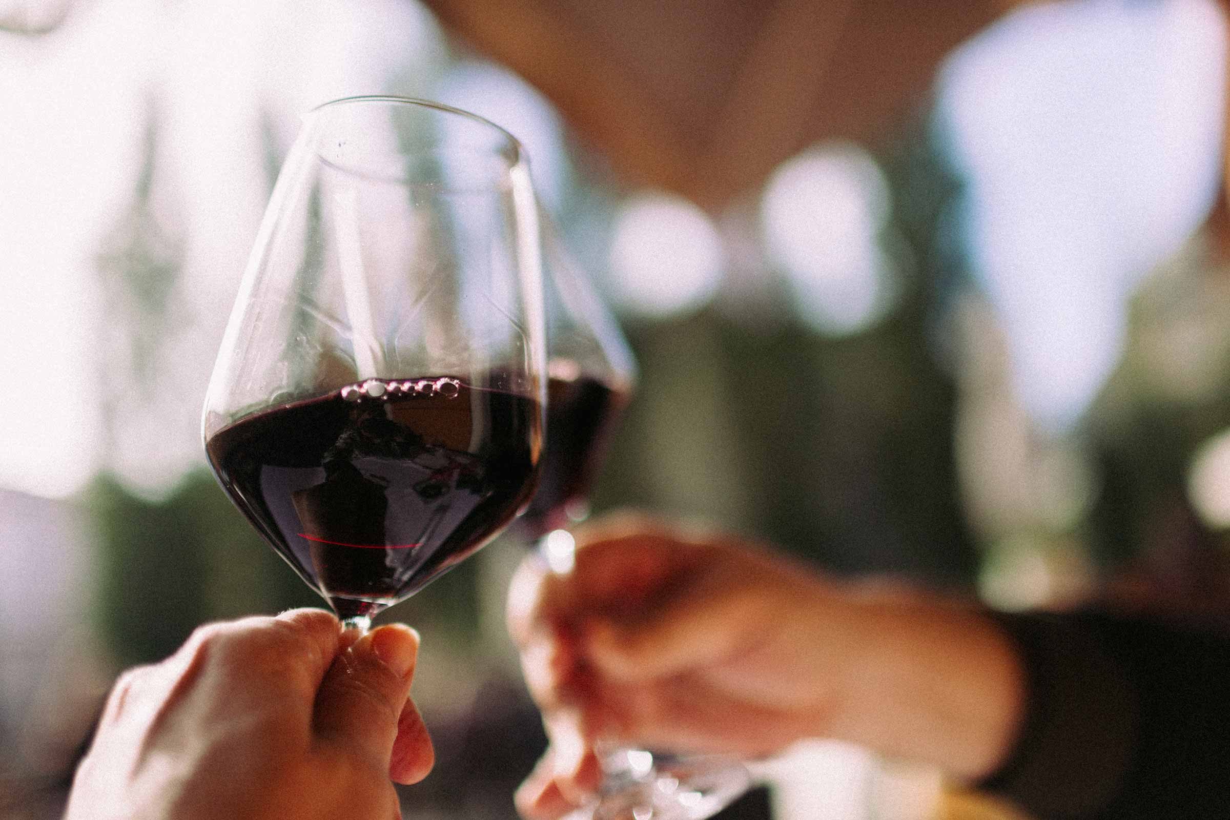 two hand holding wine glasses with red wine, clinking glasses