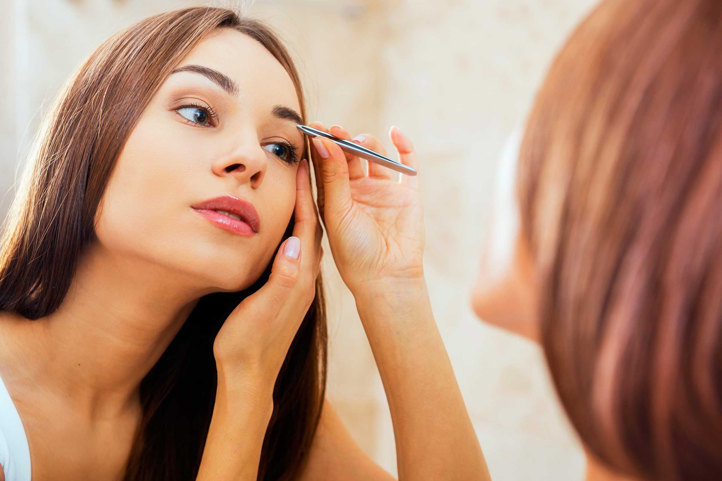 beautiful woman tweezing her eyebrows in the mirror