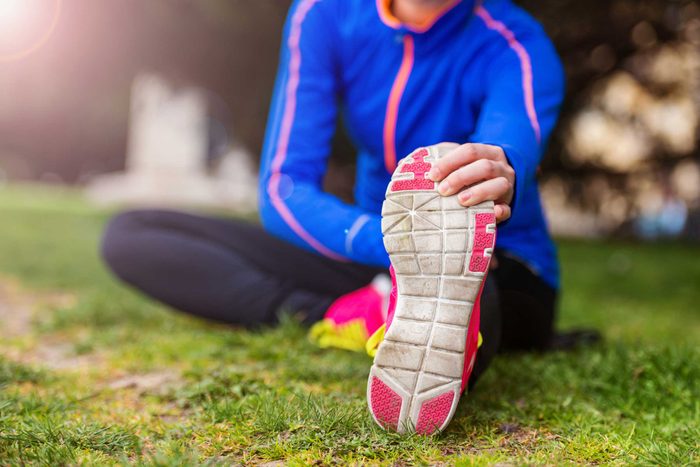 Woman in workout gear stretching her leg outdoors.