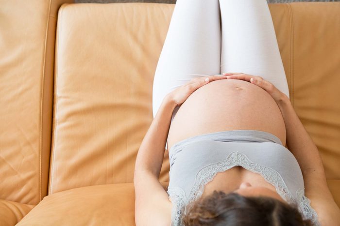 pregnant woman holding belly, sitting on couch