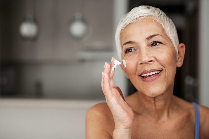 senior woman applying sunscreen to her face