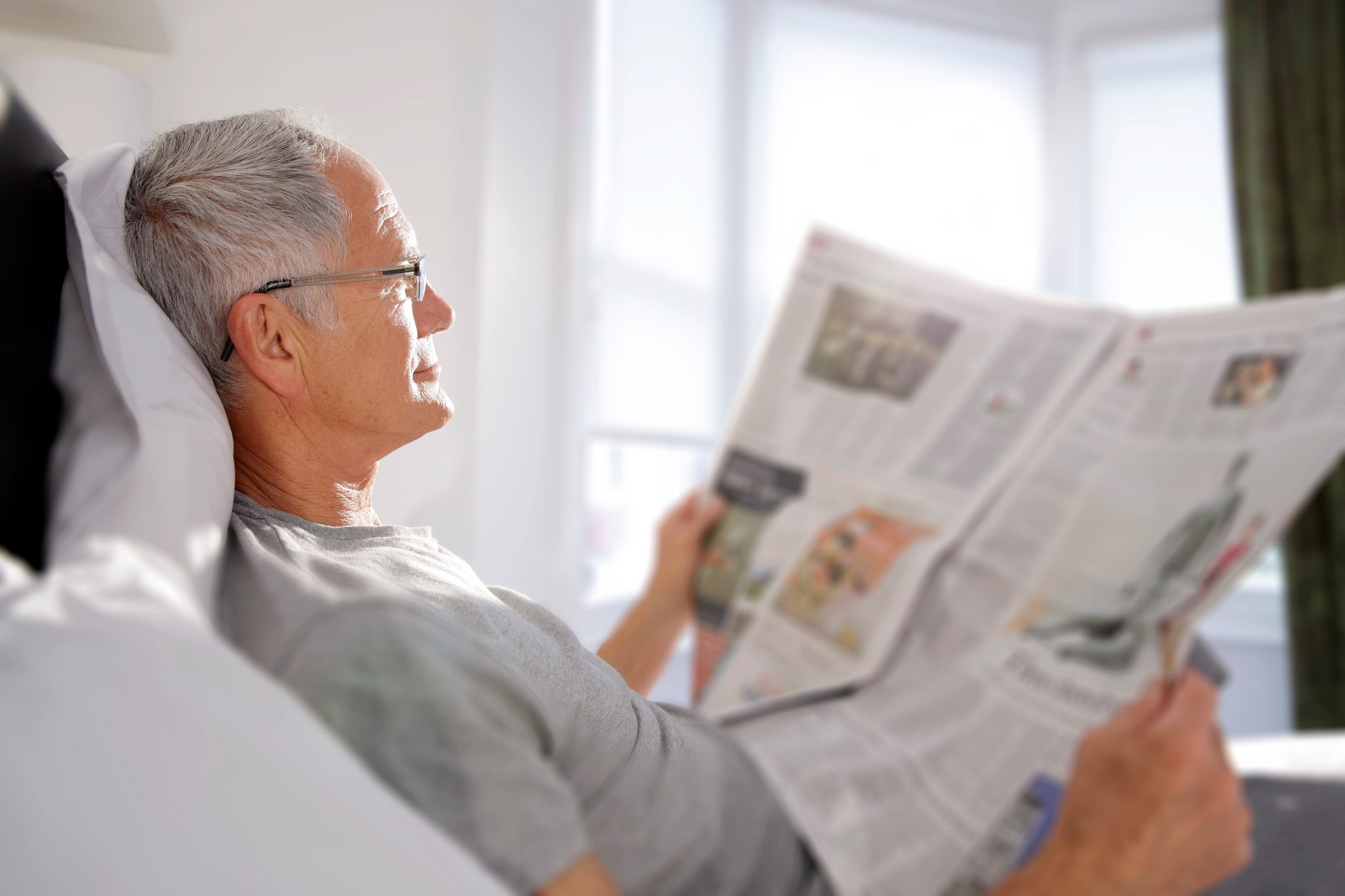 man reading newspaper in bed