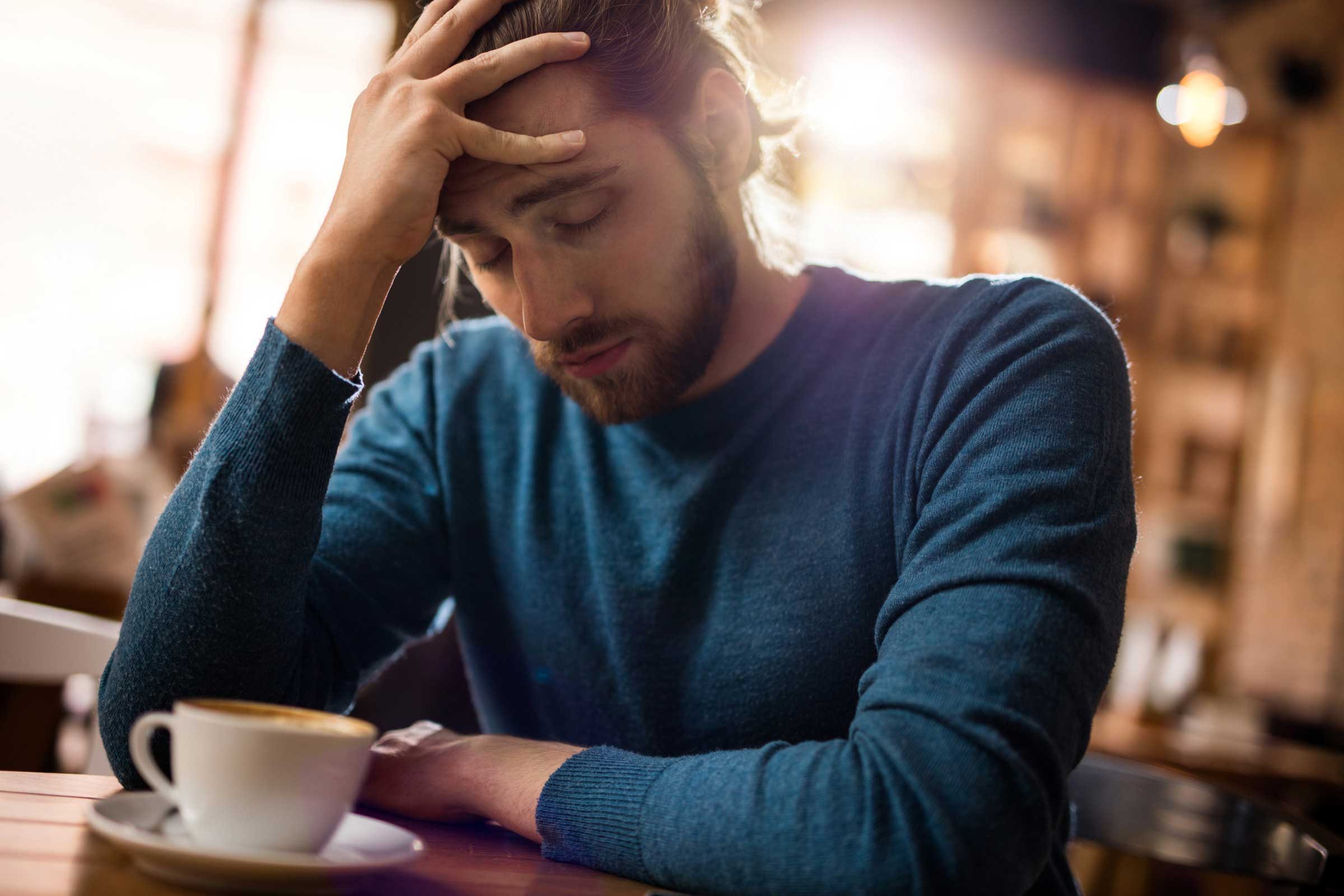 tired looking man in a coffee shop holding his head