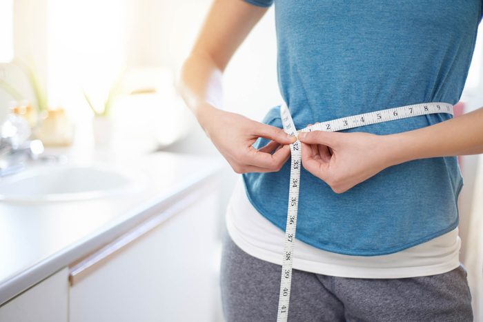woman measuring her waist with a measuring tape