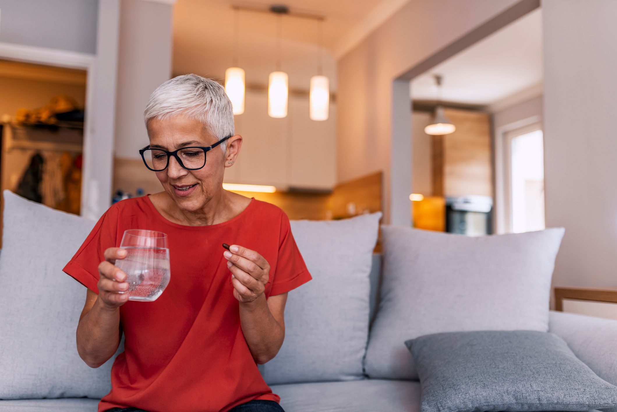 senior woman taking medication with glass of water at home