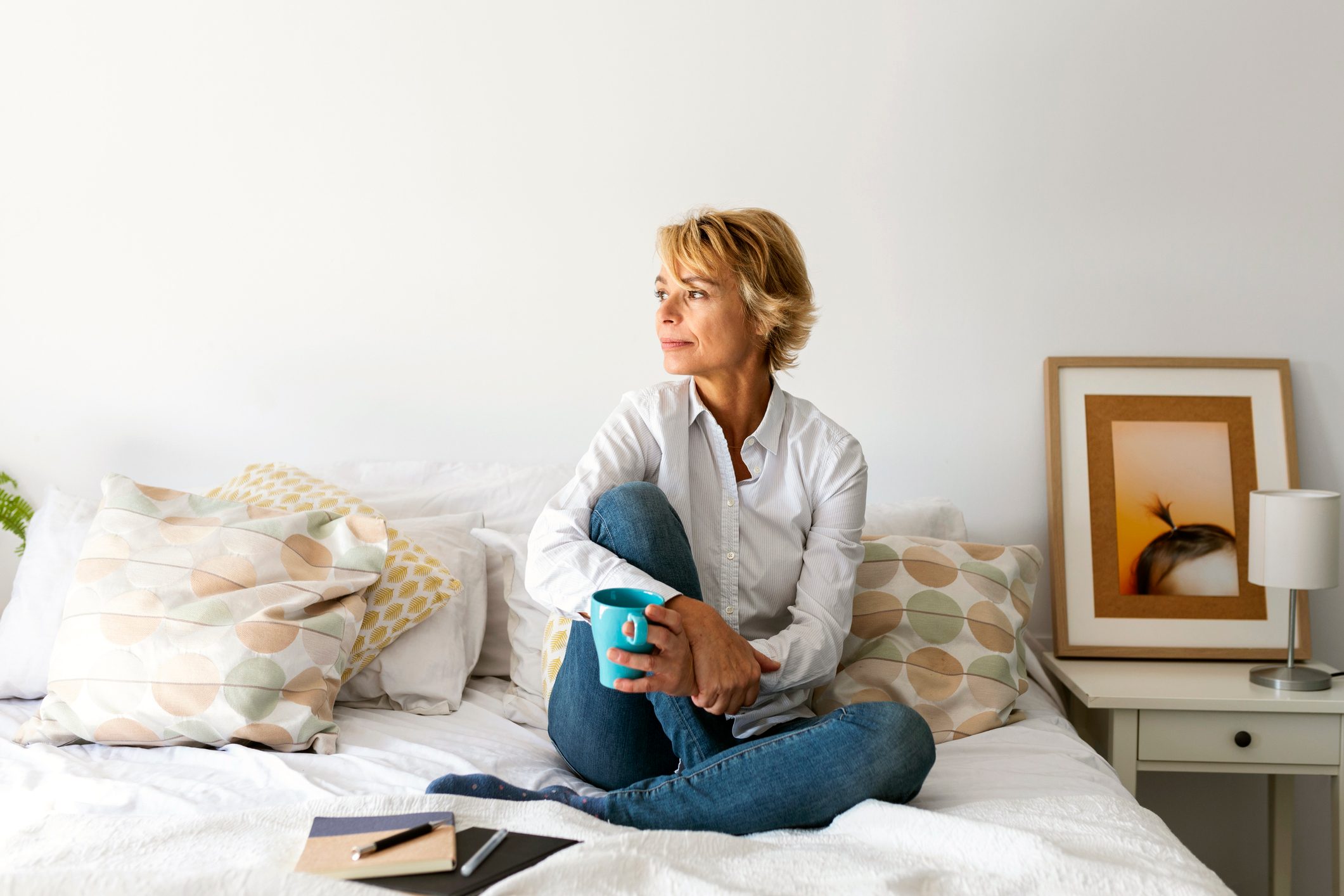 mature woman sitting on bed looking out window