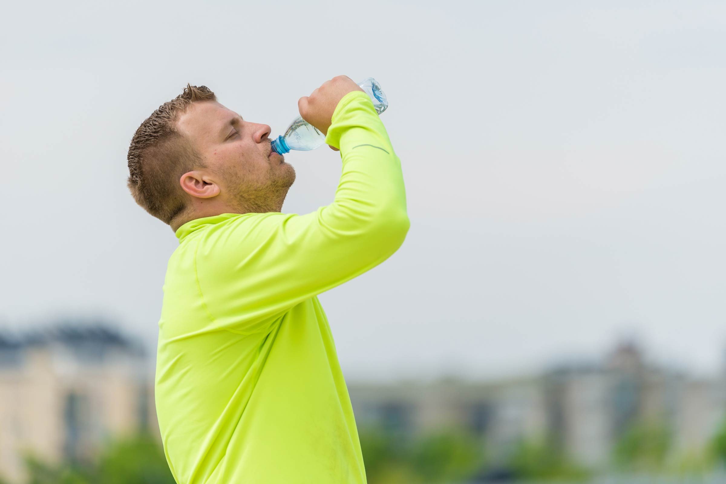 man in a yellow long-sleeve shirt drinking from a water bottle