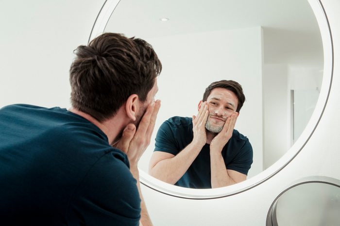 man washing face while looking in the mirror