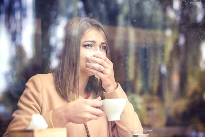 woman looking through a window holding a tissue to her nose 