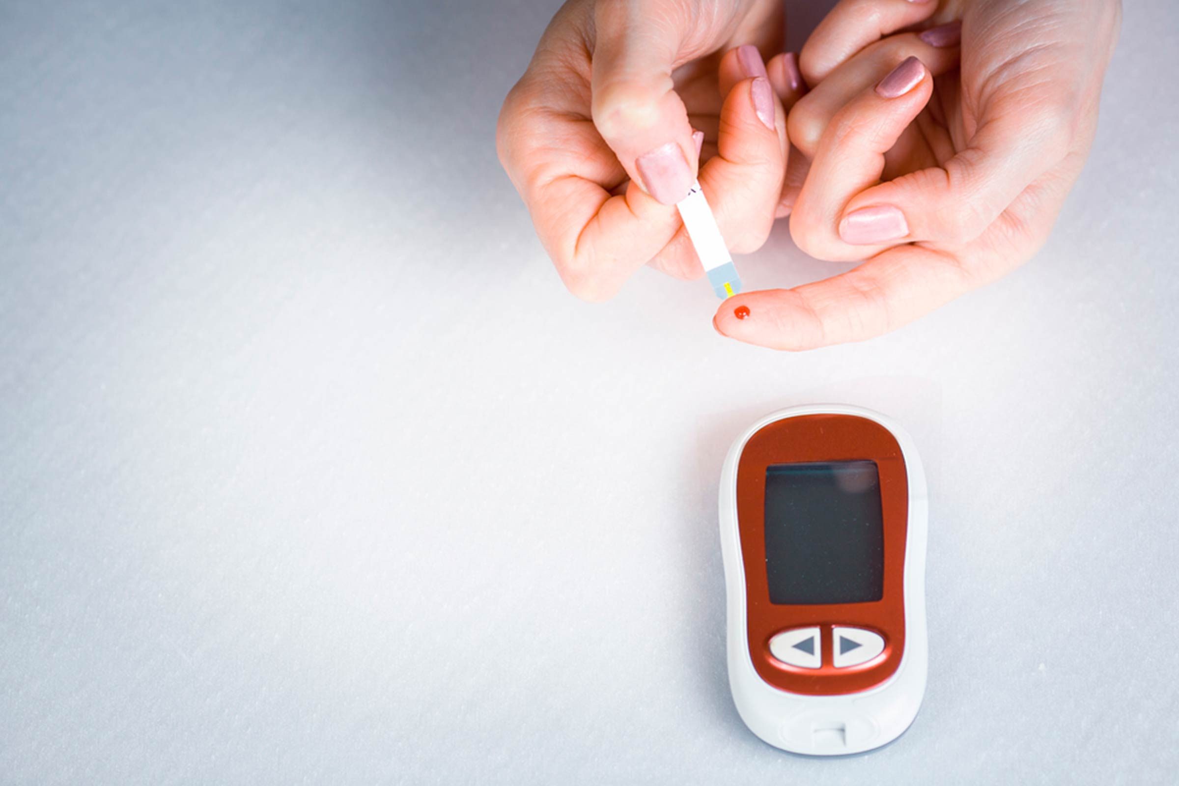 person checking blood prick on finger with test trip and glucometer