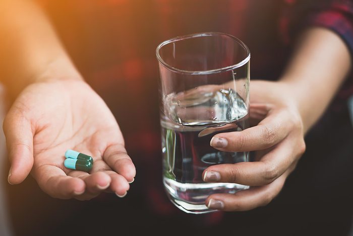woman holding water in one hand and two blue capsules in the other