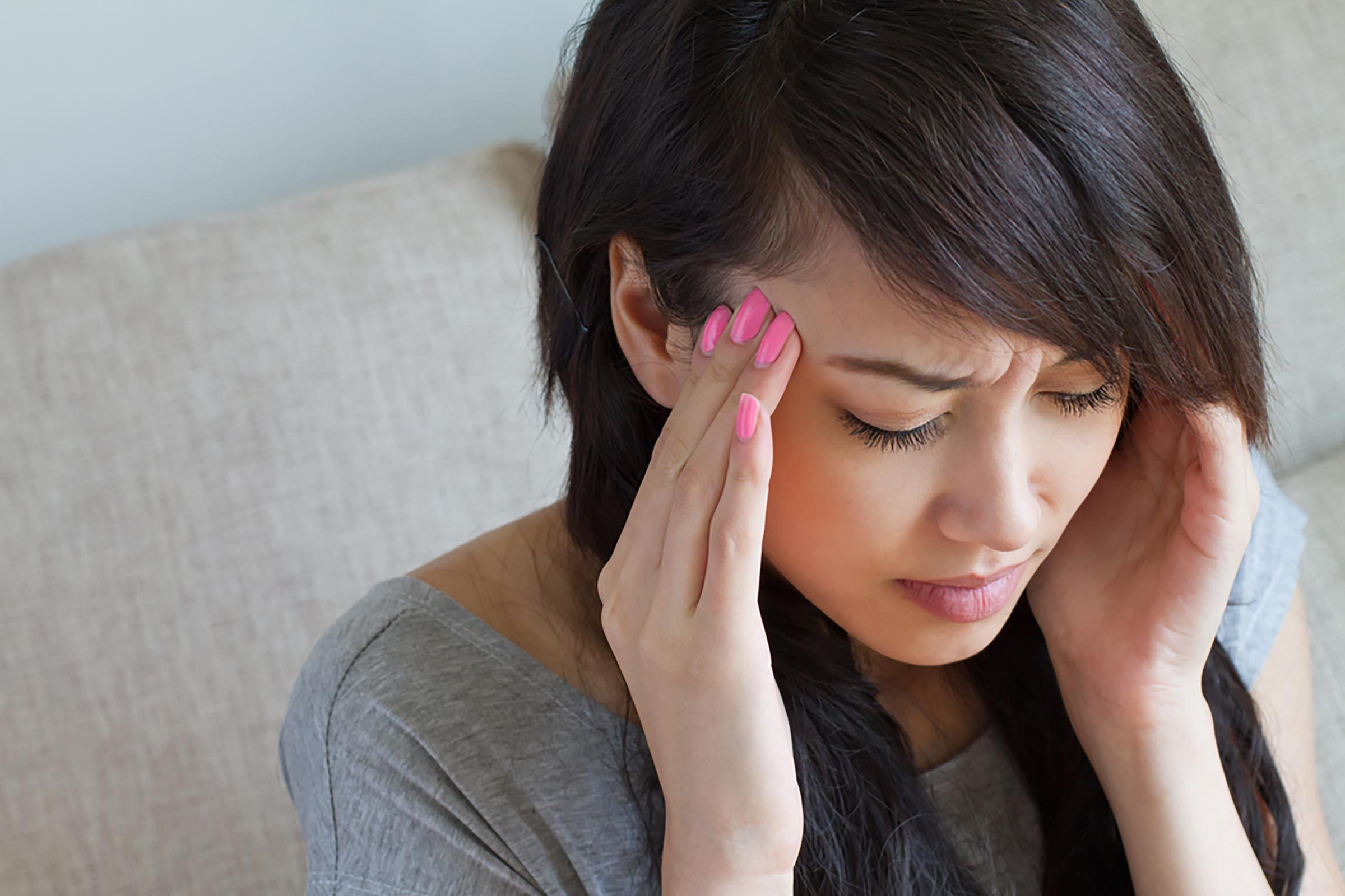Asian woman with a headache holding her hands to her temples