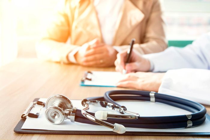 doctor writing at a desk next to a patient, stethoscope on the table