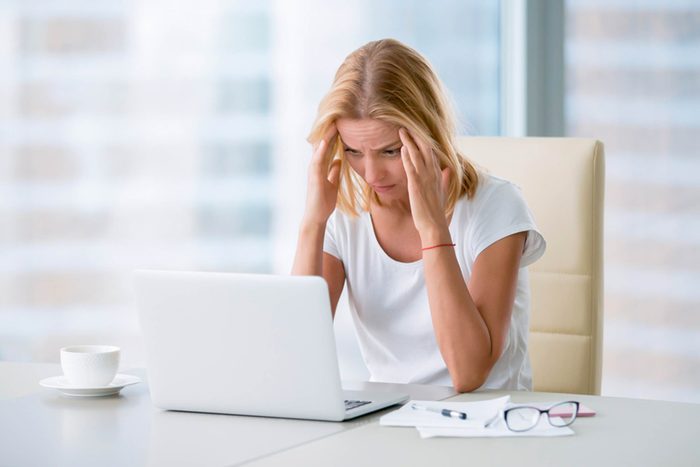 woman staring at a laptop computer and holding her temples