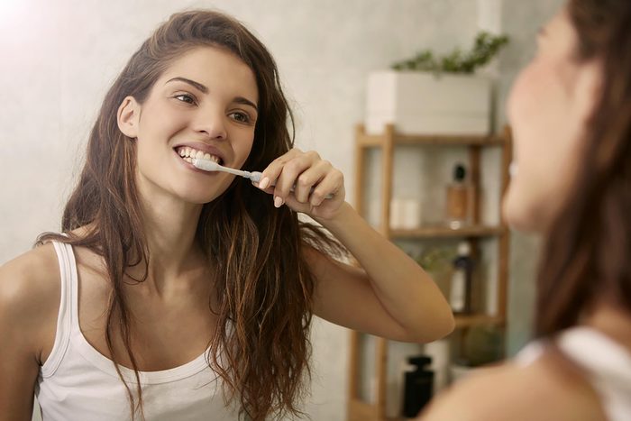 young woman brushing teeth in mirror