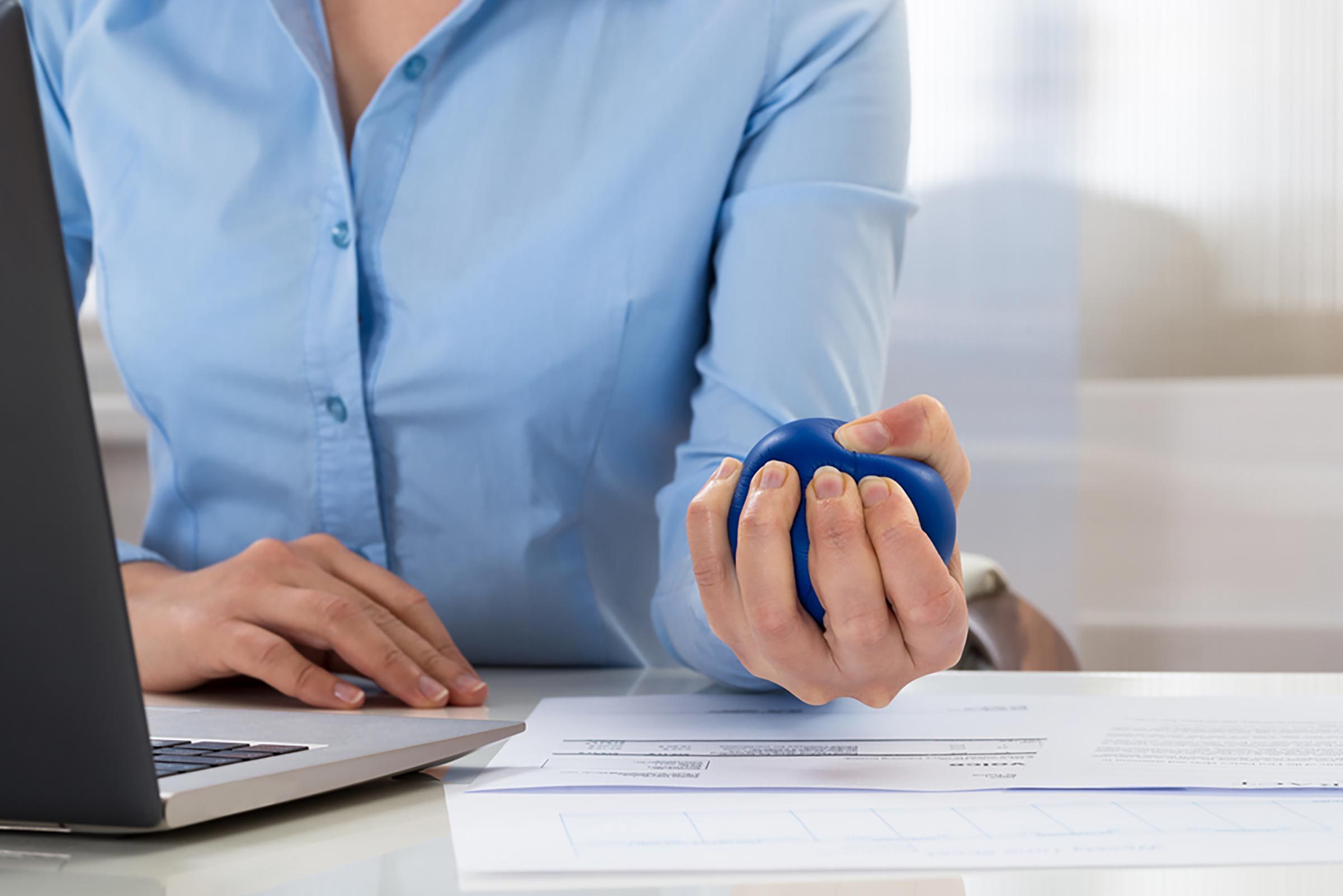 woman sitting at a laptop and squeezing a ball in left hand