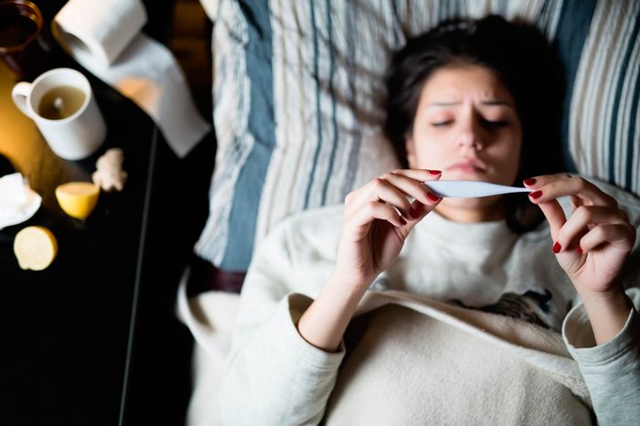worried woman in bed checking a thermometer