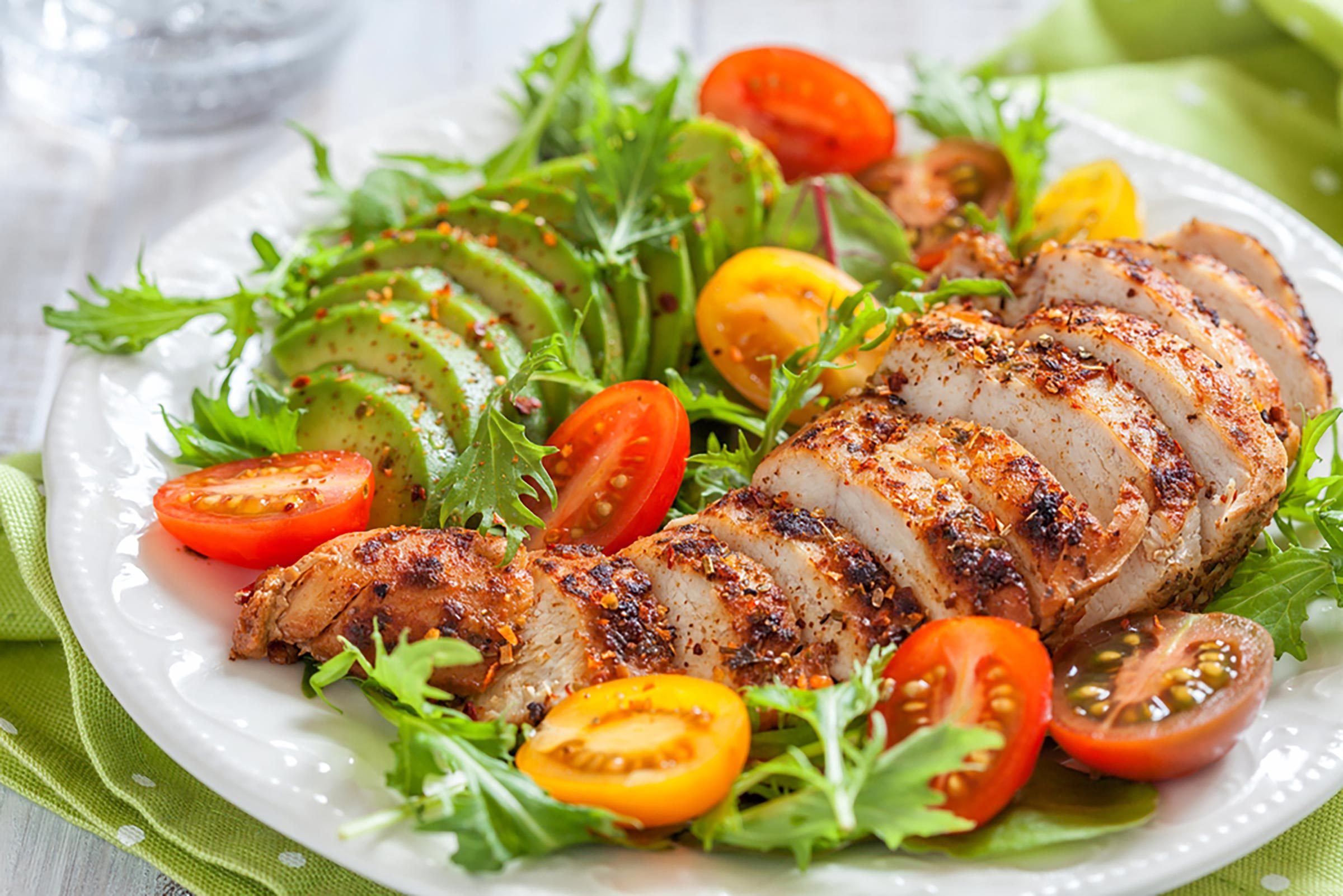 a plate of sliced meat, avocado, and tomatoes with leafy greens