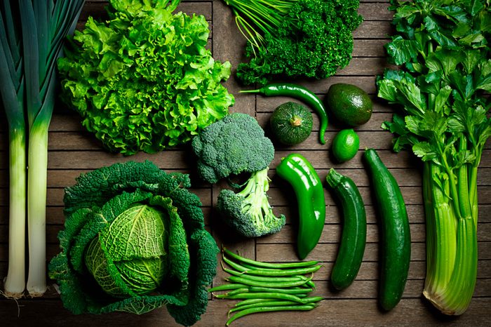 An array of dark green veggies, including leaks, lettuces, broccoli, beans, peppers, zucchini, and celery.