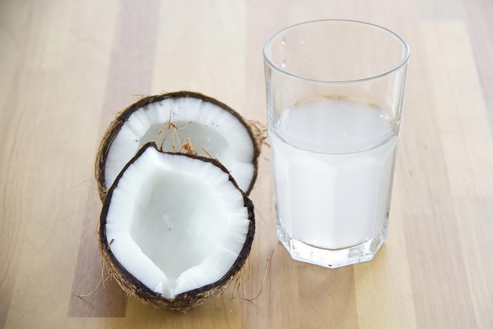 Glass of coconut water next to two halves of a coconut