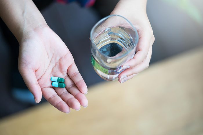person holding vitamins and a glass of water