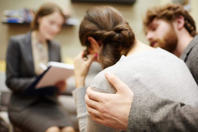 man comforting a woman in front of a therapist