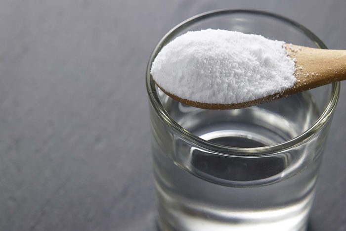 Wooden spoon of baking soda over a glass of water.