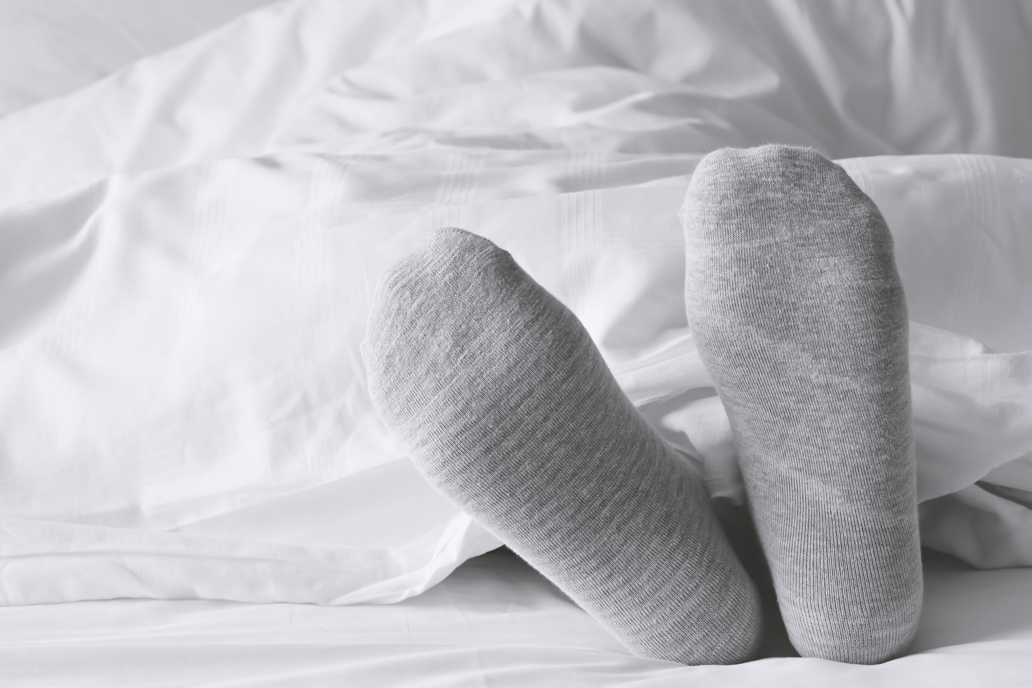 close up of gray socks on feet in white bed