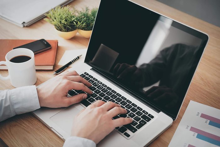 man using laptop with cup of coffee nearby