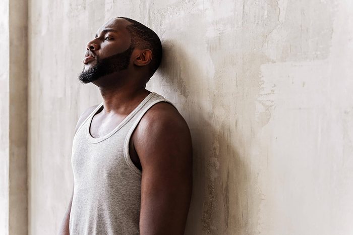 tired man in tank top leaning against wall