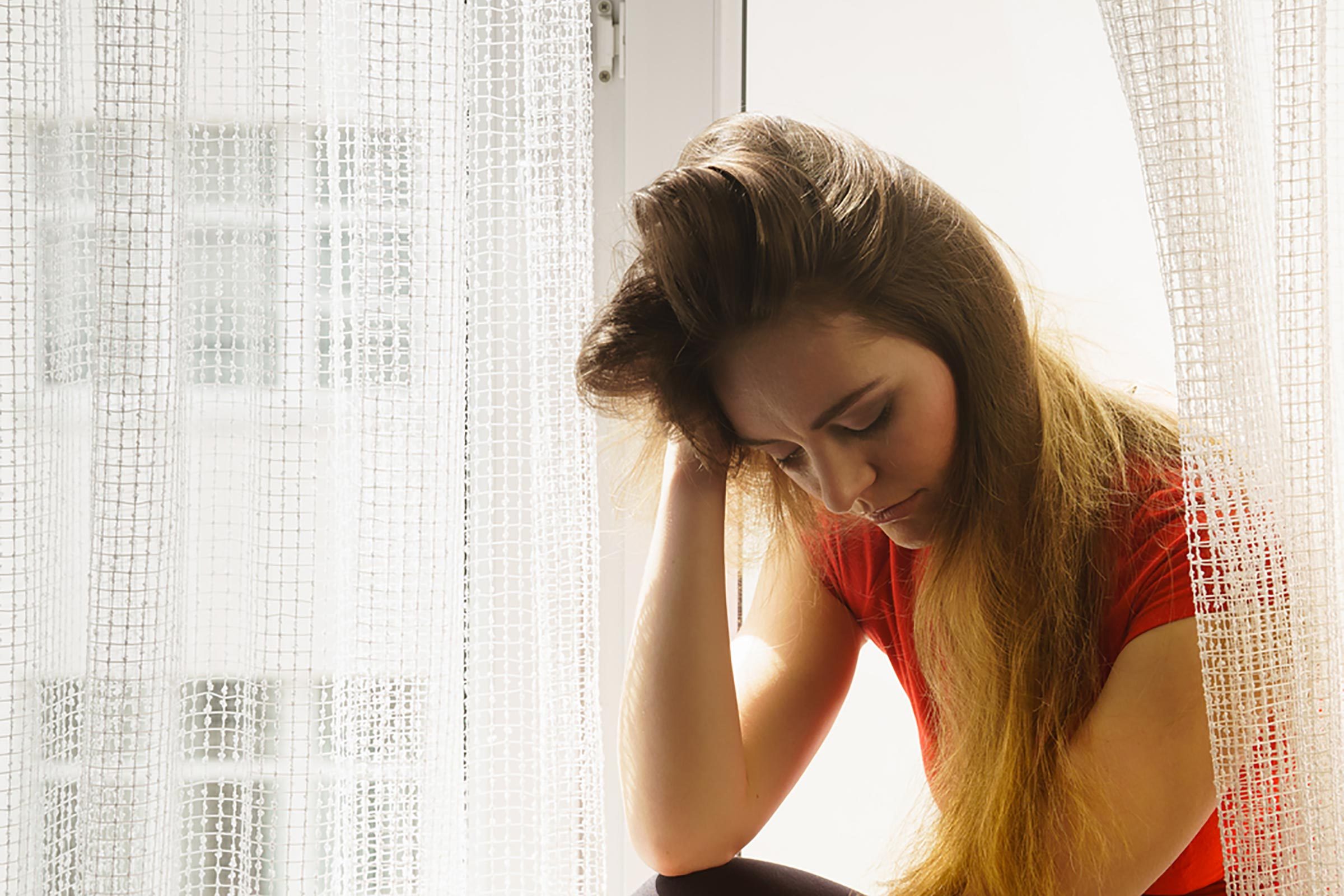 woman sitting at a window looking down and holding her head